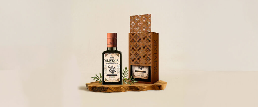 Award-winning premium olive oil packaging design for Olivixir Nikolos Collection by ABC Design, featuring an elegant dark glass bottle with heritage-style typography alongside a luxury laser-cut wooden gift box on a rustic wood base.