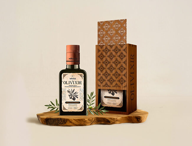 Award-winning premium olive oil packaging design for Olivixir Nikolos Collection by ABC Design, featuring an elegant dark glass bottle with heritage-style typography alongside a luxury laser-cut wooden gift box on a rustic wood base.