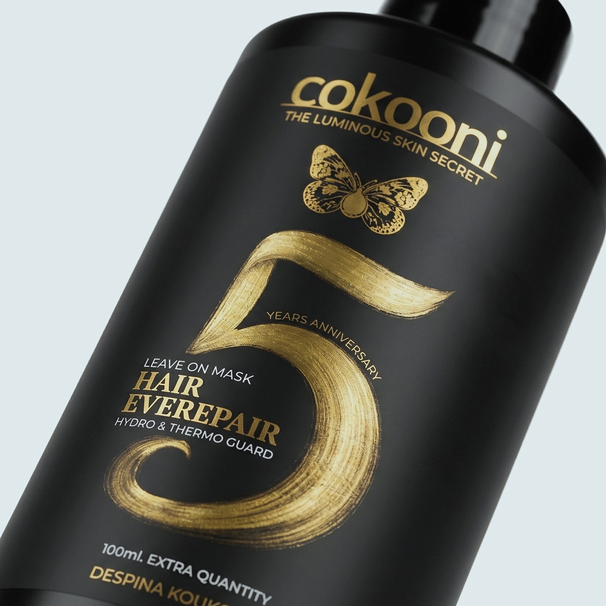 High-angle studio shot of the Cokooni premium black hair care dispenser, highlighting the sleek pump mechanism and exquisite gold anniversary lettering.
